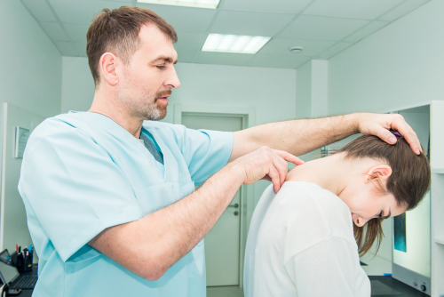 Clinician assessing a patient’s neck in a treatment room